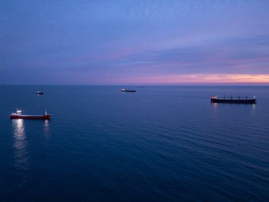 Sakin denizin üzerinde gün batımında altın ışıkla aydınlatılan kargo gemileri sakin bir deniz atmosferi yaratıyor..
