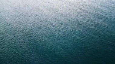 Sakin deniz sularının havadan görünüşü. Suyun yüzeyi doğal ışık altında dokulu, sakin bir kalıp oluşturarak minimalist ve barışçıl bir deniz arka planı oluşturur..