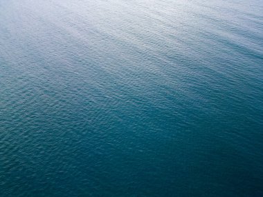 Sakin deniz sularının havadan görünüşü. Suyun yüzeyi doğal ışık altında dokulu, sakin bir kalıp oluşturarak minimalist ve barışçıl bir deniz arka planı oluşturur..