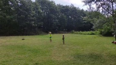 İki çocuk, ağaçlarla çevrili açık otlak bir alanda oyuncak bir uçakla oynuyor. Neşeli bir açık hava oyun sahnesi.