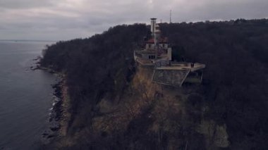 Varna yakınlarındaki Galata Burnu 'ndaki harabe kafe ve terk edilmiş deniz feneri, bir heyelandan etkilenmiş, ormanlık bir uçurum ve bulutlu bir gökyüzünün altında kayalık bir kıyı şeridi ile çevrili..