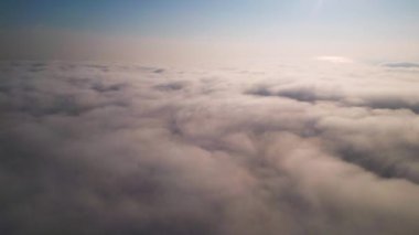 Gökyüzü yumuşak bulutlarla dolu, güneş ışığı kırılıyor, sakin ve sakin bir atmosfer yaratıyor. Puslu, kabarık katmanların havadan görünüşü, pastel renkleri rüya gibi ve ruhani bir ufukla harmanlıyor..