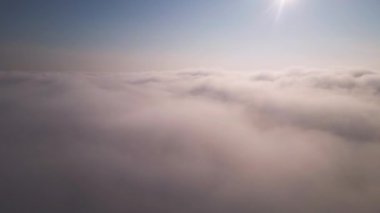 Gökyüzü yumuşak bulutlarla dolu, güneş ışığı kırılıyor, sakin ve sakin bir atmosfer yaratıyor. Puslu, kabarık katmanların havadan görünüşü, pastel renkleri rüya gibi ve ruhani bir ufukla harmanlıyor..