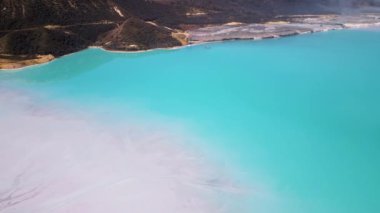 Çimento fabrikasının yanında engebeli tepelerle çevrili bir turkuaz gölet. Canlı su, çorak topraklarla çelişiyor ve çarpıcı bir çevresel etkiye sahip sanayi manzarası yaratıyor..