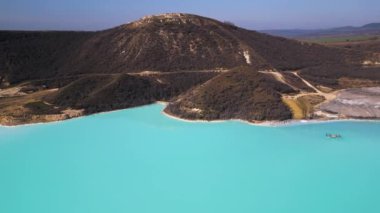 Çimento fabrikasının yanında engebeli tepelerle çevrili bir turkuaz gölet. Canlı su, çorak topraklarla çelişiyor ve çarpıcı bir çevresel etkiye sahip sanayi manzarası yaratıyor..