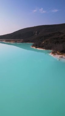 Çimento fabrikasının yanında engebeli tepelerle çevrili bir turkuaz gölet. Canlı su, çorak topraklarla çelişiyor ve çarpıcı bir çevresel etkiye sahip sanayi manzarası yaratıyor..