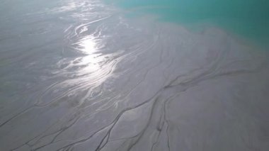 Çimento fabrikasının yanında engebeli tepelerle çevrili bir turkuaz gölet. Canlı su, çorak topraklarla çelişiyor ve çarpıcı bir çevresel etkiye sahip sanayi manzarası yaratıyor..