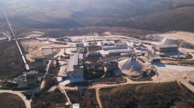 Çorak tepeler ve toprak yollarla çevrili büyük bir endüstriyel çimento fabrikası. Konveyör bantları ve depolama tesisleri, aktif üretimi ve çevresel etkilerini gözler önüne sererek bölgeye hakim durumdalar..
