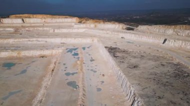 Tozlu arazide çalışan teraslı katmanlı ve ağır makineli bir açık maden ocağı. Sanayi sahasında geniş çaplı kazı süreçleri ve çevresel dönüşüm vurgulanıyor.