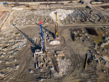 Ağır makineli sondaj ve hazırlık temelleri olan bir inşaat alanı. Yığınlar, inşaat demirleri ve çamurlu yollar zemini kaplıyor, endüstriyel temel geliştirme sürecinde ilerleme gösteriyor.