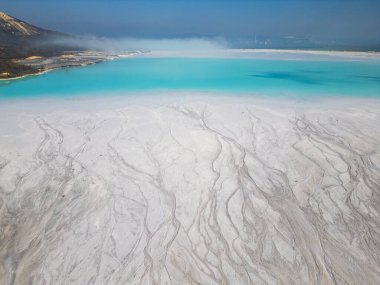 A turquoise tailings pond near a cement factory, surrounded by rugged hills. The vivid water contrasts with the barren land, creating a striking yet industrial scene of environmental impact. clipart