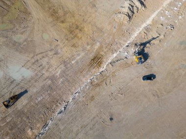 Tozlu arazide çalışan teraslı katmanlı ve ağır makineli bir açık maden ocağı. Sanayi sahasında geniş çaplı kazı süreçleri ve çevresel dönüşüm vurgulanıyor.