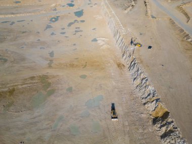 Tozlu arazide çalışan teraslı katmanlı ve ağır makineli bir açık maden ocağı. Sanayi sahasında geniş çaplı kazı süreçleri ve çevresel dönüşüm vurgulanıyor.