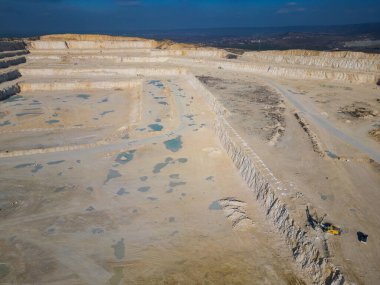 Tozlu arazide çalışan teraslı katmanlı ve ağır makineli bir açık maden ocağı. Sanayi sahasında geniş çaplı kazı süreçleri ve çevresel dönüşüm vurgulanıyor.