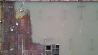 Yüksek katlı bir inşaat sahasındaki güçlendirilmiş çelik demirin üzerine beton döken ve dağıtan işçilerin yukarıdan aşağı havadan görünüşü. Bir boom pompası çimento sağlar, kentsel yapı için bir temel oluşturur.