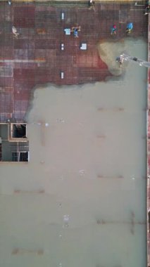 Yüksek katlı bir inşaat sahasındaki güçlendirilmiş çelik demirin üzerine beton döken ve dağıtan işçilerin yukarıdan aşağı havadan görünüşü. Bir boom pompası çimento sağlar, kentsel yapı için bir temel oluşturur.