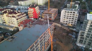 Yüksek binası olan bir inşaat alanının havadan görüntüsü. Bir beton pompa çatıya çimento dökerken, işçiler ve iskeleler ilerlemeyi gösteriyor. Etrafı modern insanlarla çevrili