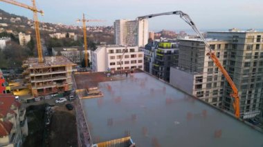 Gelişmekte olan yüksek katlı bir binanın bulunduğu aktif bir inşaat alanının havadan görüntüsü. Beton bir pompa çatıya çimento döküyor, vinçleri, iskelesi ve yapısal iskeleti var.