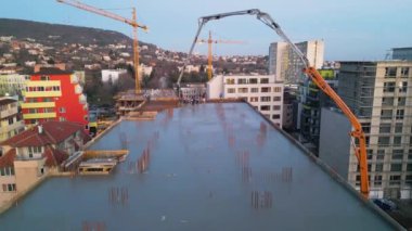 Gelişmekte olan yüksek katlı bir binanın bulunduğu aktif bir inşaat alanının havadan görüntüsü. Beton bir pompa çatıya çimento döküyor, vinçleri, iskelesi ve yapısal iskeleti var.