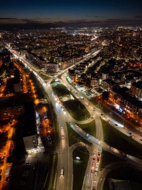 Aerial view of Varna, Bulgaria, at sunset, showcasing a vibrant cityscape with illuminated streets, moving traffic, and a glowing skyline. The coastal metropolis reflects urban energy and modern clipart