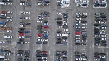 Kalabalık otoparkta sayısız farklı renk ve boyda araç açık gökyüzünün altında sıralanmıştır. Arabaların yarattığı gölgeler asfaltta desenler oluşturuyor..