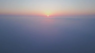 Geniş bir bulut denizinin üzerinde gün doğumu. Altın ışık, sisli gökyüzünü nazikçe aydınlatır. Yumuşak renkler ve yumuşak hareketlerle rüya gibi, sakin bir atmosfer yaratır. Hava aracı görünümü.