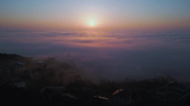 Puslu bir dağ manzarası üzerinde büyüleyici bir gün doğumu. Altın ışık, yuvarlanan bulutları aydınlatıyor. Sakin atmosfer, orman siluetlerini yumuşak sabah renkleriyle harmanlıyor ve nefes kesici bir hava yaratıyor.