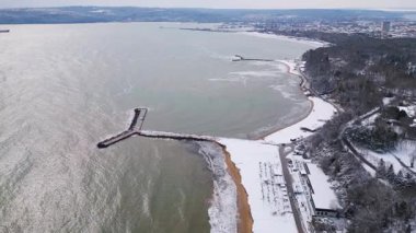 Bulgaristan 'ın Varna kentinde kış manzarası, karla kaplı bir plaj, sakin bir deniz ve kıyı rıhtımı bulunuyor. Mevsimsel dönüşümün güzelliğini gözler önüne seren kışın ve deniz kıyısının eşsiz bir zıtlığı..