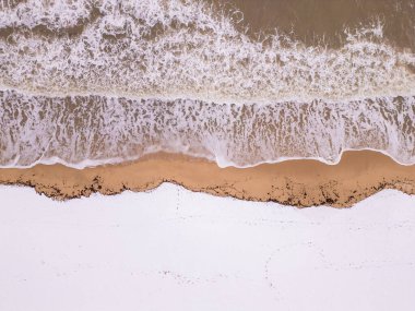 Kışın köpüklü okyanus dalgalarının karlı topraklarla buluştuğu kışa ait bir perspektif. Dokuların ve renklerin birleşimi doğadaki mevsimsel geçişlerin güzelliğini vurgular.