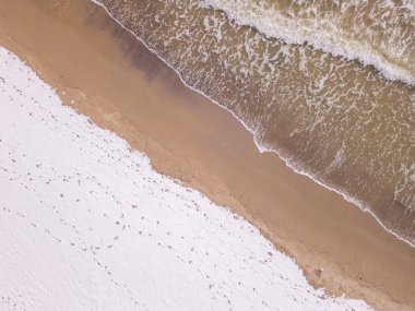 Kışın köpüklü okyanus dalgalarının karlı topraklarla buluştuğu kışa ait bir perspektif. Dokuların ve renklerin birleşimi doğadaki mevsimsel geçişlerin güzelliğini vurgular.