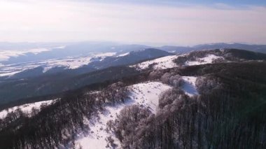 Bulgaristan 'daki karla kaplı Balkan Dağları' nın havadan görünüşü. Kış manzarasında yuvarlanan tepeler, don kaplı ağaçlar ve açık mavi bir gökyüzü yer alır. Yürüyüşçüler sakin çölde yürürler.