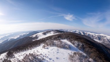 Bulgaristan 'daki karla kaplı Balkan Dağları' nın havadan görünüşü. Kış manzarasında yuvarlanan tepeler, don kaplı ağaçlar ve açık mavi bir gökyüzü yer alır. Yürüyüşçüler sakin çölde yürürler.