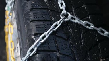 Buzlu yollarda daha iyi yol tutuşu için metal kar zincirleri olan bir kış lastiğinin yakın çekimi. Ayrıntılı ayak izleri ve güçlü bağlantılar aşırı kış koşullarında güvenlik ve istikrarı vurguluyor..