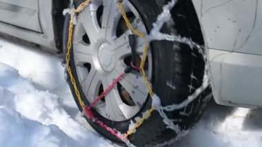 Kar zincirleriyle donatılmış bir araba karlı arazide yol alır. Yakından bakınca metal bağlantıların lastiği kavradığını görüyoruz. Buz gibi havada güvenli kış yolculukları için yol tutuşu ve istikrarı sağlıyor..