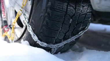 Derin karları tutan kar zincirleri olan bir kış lastiğinin yakın çekimi. Ayrıntılı lastik izleri ve metal bağlantılar sert kış koşullarında güvenli sürüş için yol tutuşu ve istikrar sağlar..