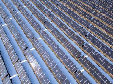 Dağınık evler ve ağaçlarla çevrili kırsal bir arazide karla kaplı büyük bir güneş çiftliğinin havadan görünüşü. Güneş panelleri beyaz zemine karşı kontrastlı, yenilenebilir enerji sergiliyor