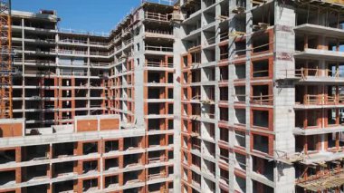 Güneşli bir günde yüksek katlı bir binanın inşaatı. Yapılar, beton iskelet, vinç ve iskelet parlak güneş ışığıyla yıkanarak kentsel gelişimi vurguluyor..