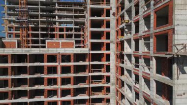 Güneşli bir günde yüksek katlı bir binanın inşaatı. Yapılar, beton iskelet, vinç ve iskelet parlak güneş ışığıyla yıkanarak kentsel gelişimi vurguluyor..