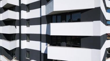 Siyah panelleri ve beyaz balkonları olan, temiz mimari çizgileri ve çağdaş kentsel tasarımı vurgulayan modern bir konut binasının insansız hava aracı görüntüsü..