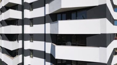 Siyah panelleri ve beyaz balkonları olan, temiz mimari çizgileri ve çağdaş kentsel tasarımı vurgulayan modern bir konut binasının insansız hava aracı görüntüsü..
