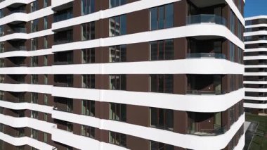 Kahverengi panelleri ve beyaz balkonları olan, temiz mimari çizgileri ve çağdaş kentsel tasarımı ön plana çıkaran modern bir konut binasının insansız hava aracı görüntüsü..