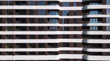 Kahverengi panelleri ve beyaz balkonları olan, temiz mimari çizgileri ve çağdaş kentsel tasarımı ön plana çıkaran modern bir konut binasının insansız hava aracı görüntüsü..