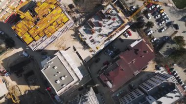 İnşaat alanında kentsel bir alanda parlak güneş ışığı altında canlı malzeme ve ekipmanlar sergileniyor. Havadan yukarıdan aşağıya görünüm.
