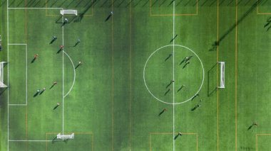 Yeşil bir sahada oyuncuların ve ekipmanların görüldüğü bir futbol antrenmanının yukarıdan aşağı görünümü.