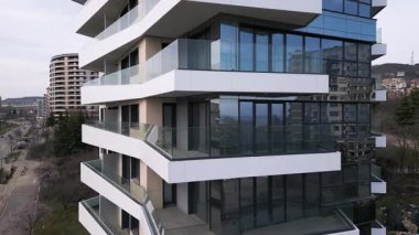 Siyah panelleri ve beyaz balkonları olan, temiz mimari çizgileri ve çağdaş kentsel tasarımı vurgulayan modern bir konut binasının insansız hava aracı görüntüsü..