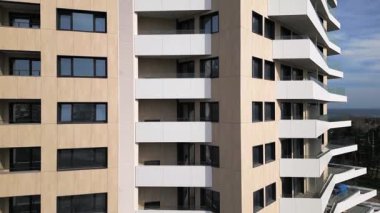 Kahverengi panelleri ve beyaz balkonları olan, temiz mimari çizgileri ve çağdaş kentsel tasarımı ön plana çıkaran modern bir konut binasının insansız hava aracı görüntüsü..