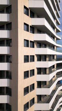 Kahverengi panelleri ve beyaz balkonları olan, temiz mimari çizgileri ve çağdaş kentsel tasarımı ön plana çıkaran modern bir konut binasının insansız hava aracı görüntüsü..