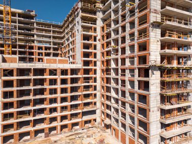 Güneşli bir günde yüksek katlı bir binanın inşaatı. Yapılar, beton iskelet, vinç ve iskelet parlak güneş ışığıyla yıkanarak kentsel gelişimi vurguluyor..