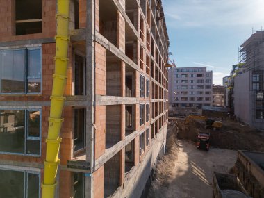 Güneşli bir günde yüksek katlı bir binanın inşaatı. Yapılar, beton iskelet, vinç ve iskelet parlak güneş ışığıyla yıkanarak kentsel gelişimi vurguluyor..