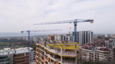 İnşaat halindeki vinçleri yüksek bir binanın havadan görüntüsü. Tamamlanmamış yapıda açık tuğlalar, beton sütunlar ve iskeleler var..